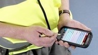 A man in high-vis vest with a mobile phone and touch screen pen carrying out a fire risk assessment.